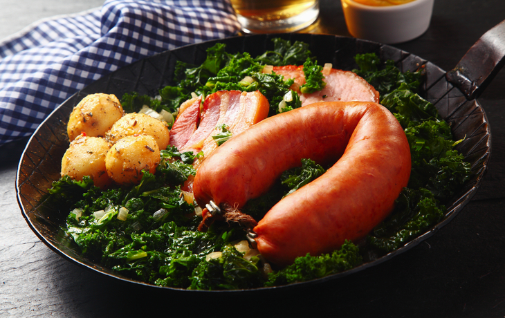Grünkohl mit Pinkelwurst und Kartoffeln in einer Pfanne serviert.