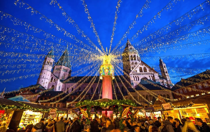 Weihnachtsmarkt bei Nacht mit Lichterketten und Kathedrale im Hintergrund.