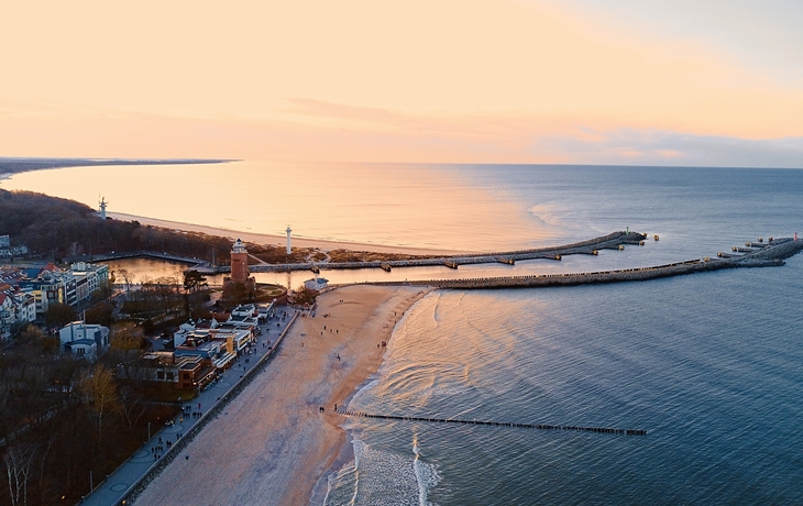 Luftaufnahme von Kolberg im Winter bei Sonnenuntergang, mit Strand, Ozean und Stadt.