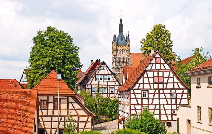 Fachwerkhäuser in einem malerischen deutschen Dorf mit einem Kirchturm im Hintergrund.