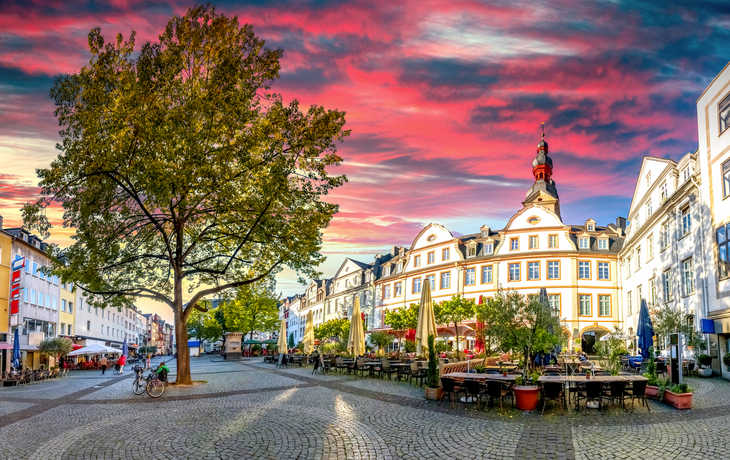 Historischer Marktplatz mit Tischen, Stühlen und farbenprächtigem Sonnenuntergangshimmel.