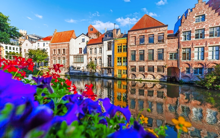 Häuser am Kanal mit bunten Blumen im Vordergrund, klarer Himmel.