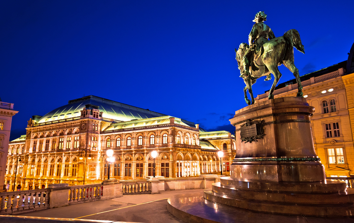 Reiterstatue im Vordergrund mit einem großen, beleuchteten Gebäude im Hintergrund bei Nacht.