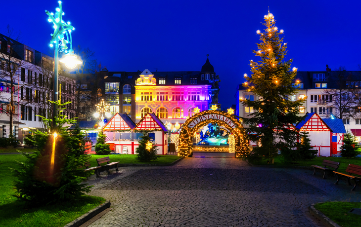 Weihnachtsmarkt am Abend mit bunten Lichtern und geschmücktem Weihnachtsbaum
