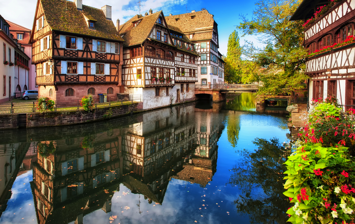 Fachwerkhäuser am Kanal in Straßburg, Elsass, mit Brücke im Hintergrund.