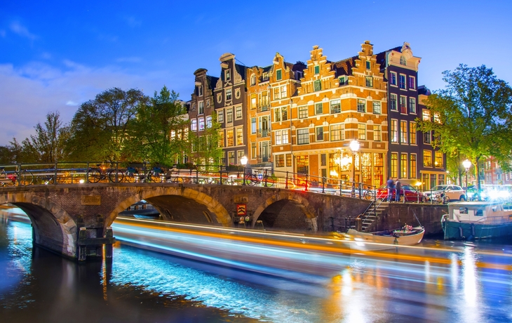 Kanal mit beleuchteter Brücke und historischen Gebäuden bei Abenddämmerung.