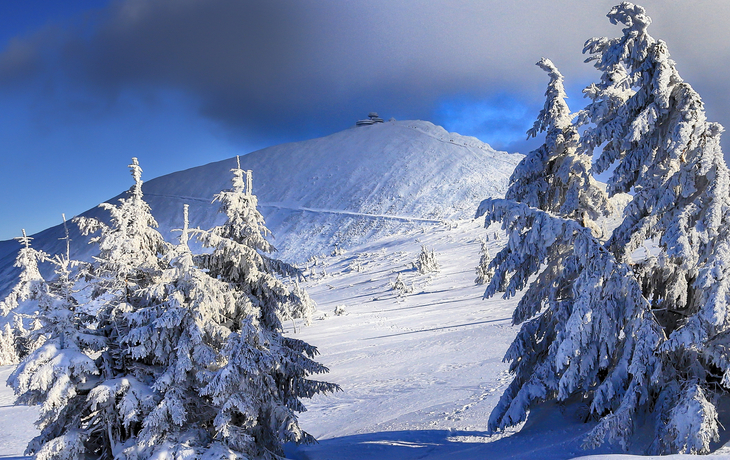 Verschneite Berglandschaft mit der Schneekoppe im Hintergrund unter blauem Himmel.