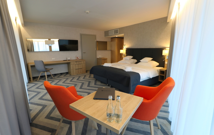 Modernes Hotelzimmer mit Doppelbett, Schreibtisch, zwei Sesseln und Tisch.