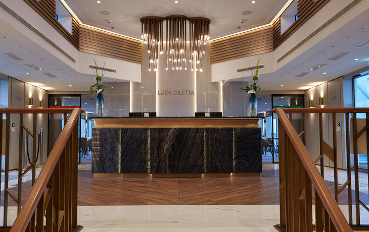 Lobby eines eleganten Schiffsrestaurants mit Treppen und moderner Dekoration.
