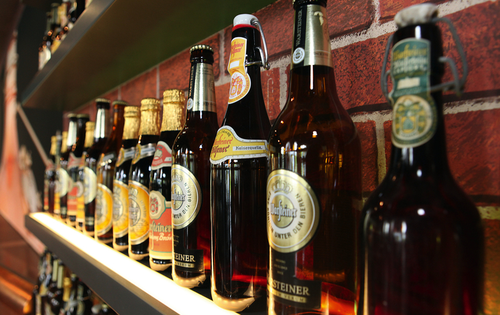 Eine Reihe von Warsteiner Bierflaschen auf einem Regal vor einer Ziegelwand.